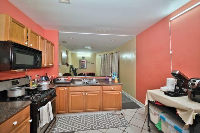 6237 N Mozart St, Chicago, IL 60659 - kitchen with light tile patterned floors, a peninsula, dark countertops, black appliances, and a sink