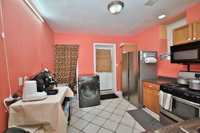 6237 N Mozart St, Chicago, IL 60659 - kitchen featuring washer / clothes dryer, light tile patterned floors, dark countertops, appliances with stainless steel finishes, and brown cabinetry