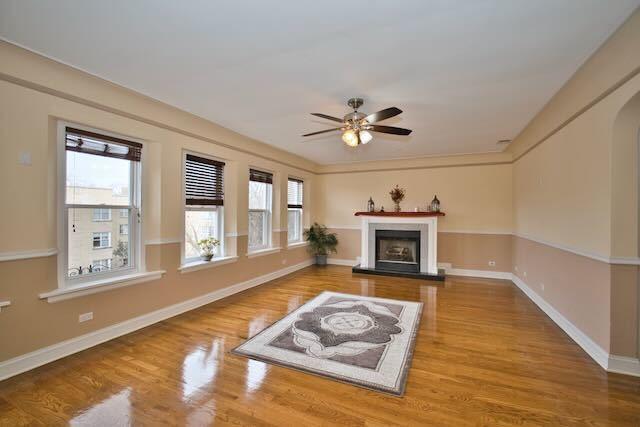 6237 N Mozart St, Chicago, IL 60659 - living room featuring baseboards, arched walkways, a fireplace with raised hearth, ceiling fan, and wood finished floors