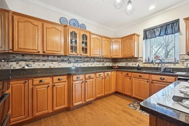 kitchen featuring light wood-style flooring, a sink, crown molding, and brown cabinetry