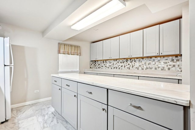 kitchen with light countertops, baseboards, backsplash, marble finish floor, and freestanding refrigerator