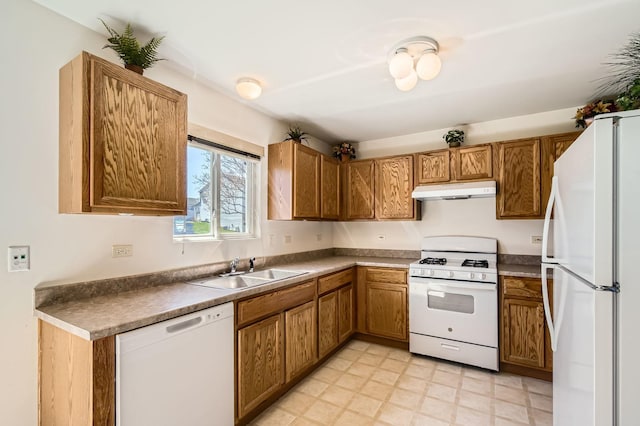 kitchen with a sink, dark countertops, white appliances, under cabinet range hood, and brown cabinets