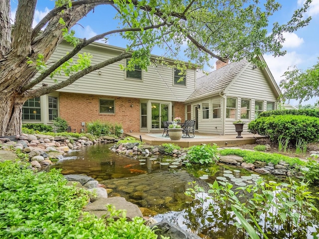 2 Stirrup Cup Ct, Saint Charles, IL 60174 - rear view of house with a small pond, brick siding, a chimney, and a patio area
