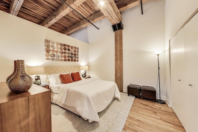 bedroom with a closet, baseboards, wood ceiling, beamed ceiling, and light wood finished floors