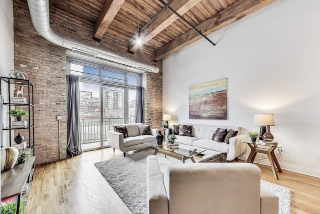 living area with beamed ceiling, brick wall, light wood-style floors, and a towering ceiling