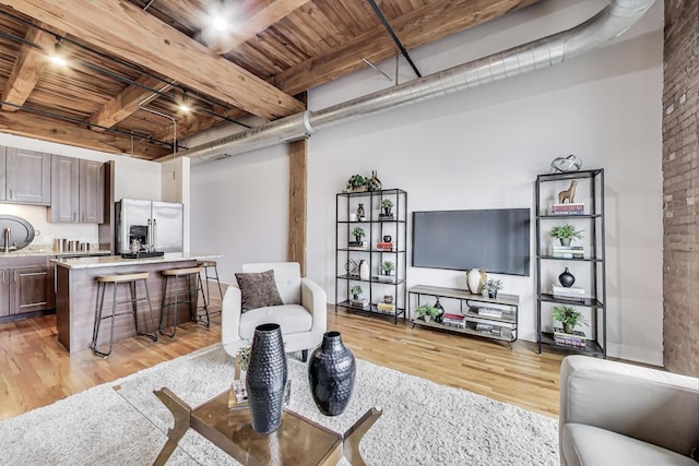 living area featuring brick wall, wooden ceiling, light wood-type flooring, and beamed ceiling