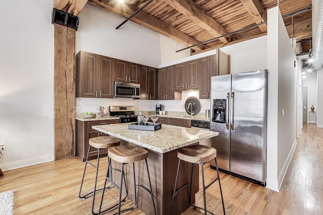 kitchen with beamed ceiling, light wood-type flooring, appliances with stainless steel finishes, and a kitchen bar