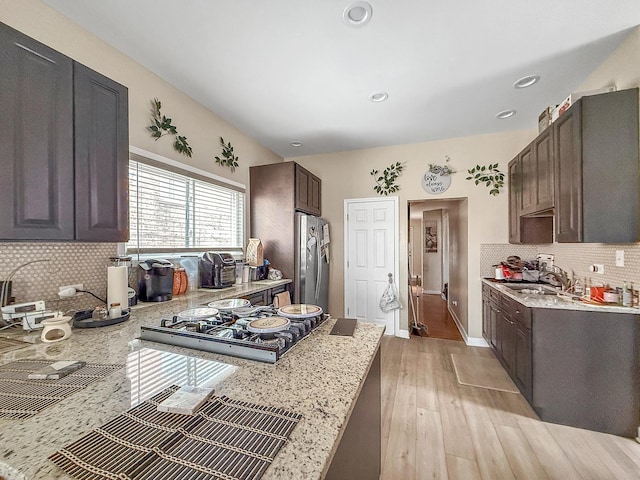 kitchen with light wood-type flooring, stainless steel fridge with ice dispenser, a sink, dark brown cabinets, and stovetop