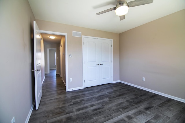 unfurnished bedroom with dark wood-type flooring, a closet, baseboards, and visible vents
