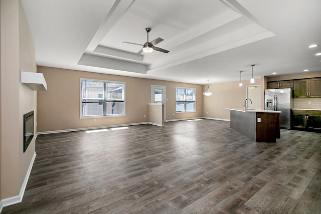 unfurnished living room with a raised ceiling, ceiling fan, dark wood-style flooring, and a sink