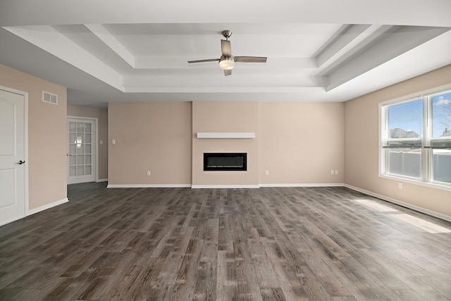 unfurnished living room featuring dark wood-type flooring, visible vents, a ceiling fan, and a raised ceiling