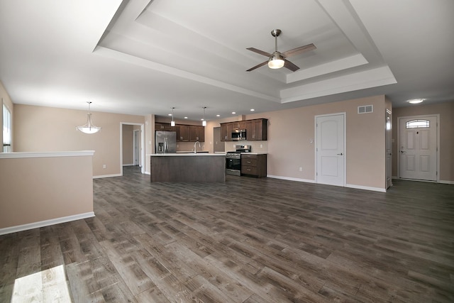 unfurnished living room featuring ceiling fan, visible vents, a sink, a raised ceiling, and baseboards