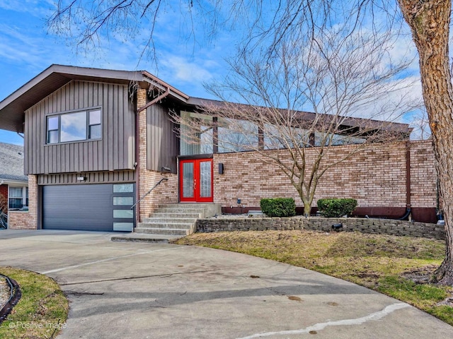tri-level home with board and batten siding, driveway, french doors, a garage, and brick siding