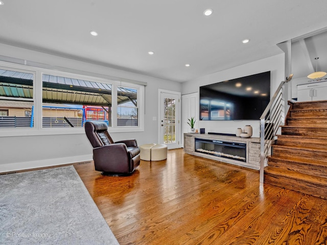 living area featuring visible vents, wood finished floors, stairway, a glass covered fireplace, and recessed lighting