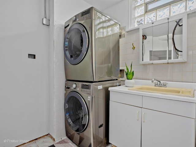 laundry room with a sink, tile walls, laundry area, and stacked washer and dryer