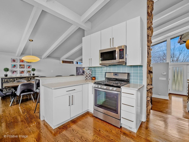 kitchen featuring tasteful backsplash, light countertops, light wood finished floors, a peninsula, and stainless steel appliances