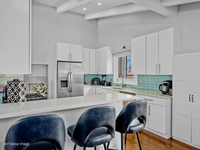 kitchen featuring decorative backsplash, beam ceiling, a kitchen breakfast bar, stainless steel refrigerator with ice dispenser, and a sink