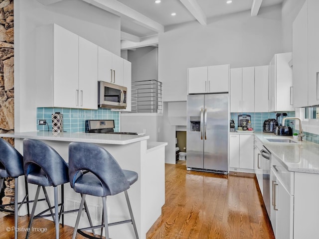 kitchen with appliances with stainless steel finishes, tasteful backsplash, beam ceiling, a sink, and a peninsula