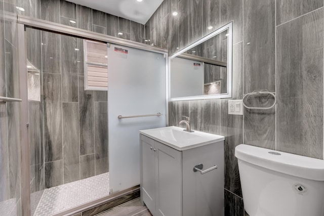 bathroom with toilet, vanity, tiled shower, and tile walls