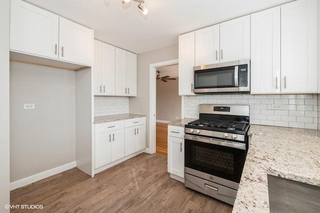 kitchen with light wood-type flooring, decorative backsplash, light stone counters, white cabinets, and appliances with stainless steel finishes
