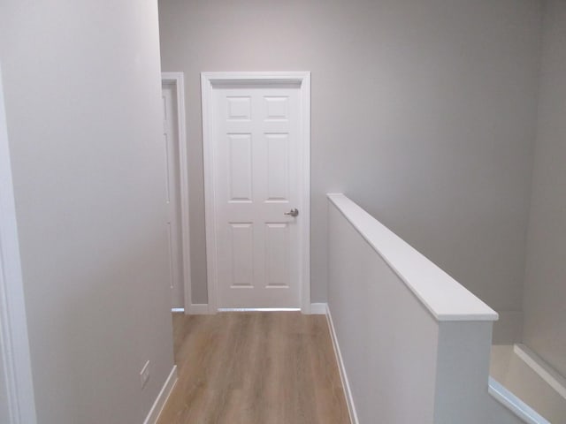 hallway with baseboards, an upstairs landing, and light wood-style floors