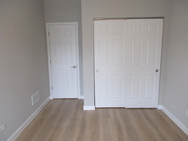 unfurnished bedroom featuring baseboards, visible vents, a closet, and wood finished floors