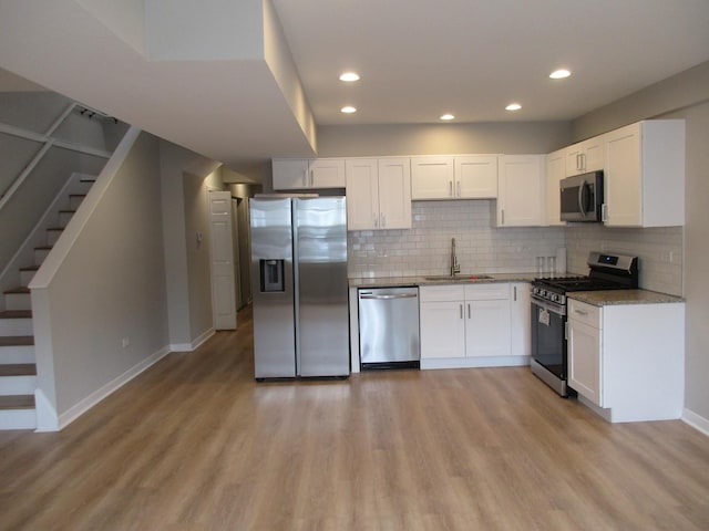 kitchen featuring stainless steel appliances, a sink, light wood finished floors, white cabinets, and light stone countertops