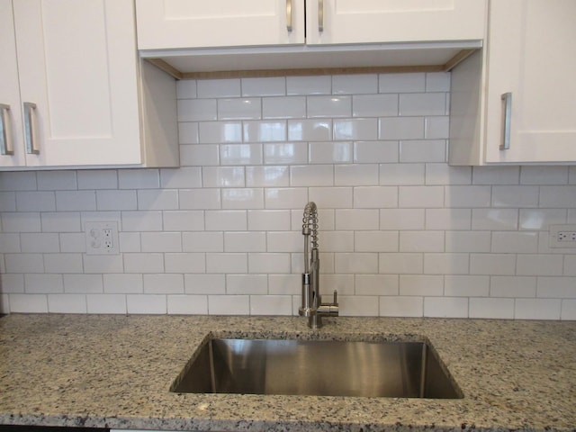 kitchen featuring decorative backsplash, white cabinetry, a sink, and light stone counters
