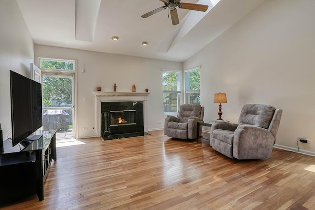 living room featuring light wood-style floors, a ceiling fan, a premium fireplace, high vaulted ceiling, and baseboards