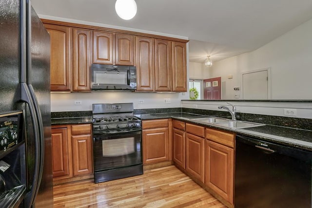 kitchen featuring black appliances, a sink, light wood-style floors, dark stone counters, and brown cabinetry