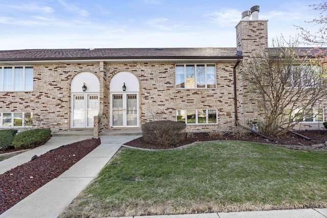view of front of home with brick siding, french doors, a chimney, and a front yard