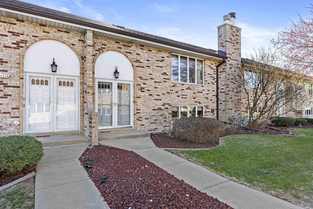 property entrance featuring a chimney, french doors, a yard, and brick siding