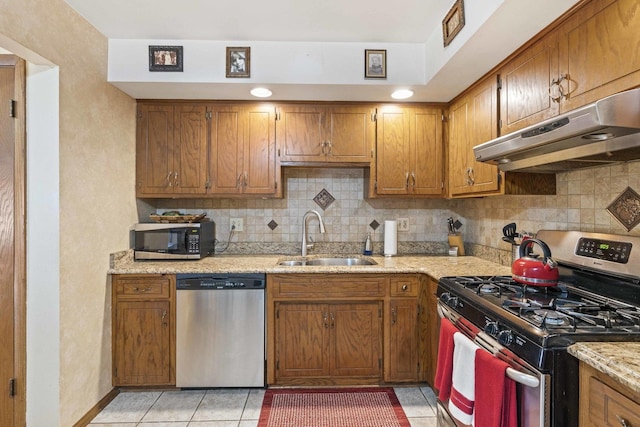 kitchen featuring tasteful backsplash, under cabinet range hood, light tile patterned flooring, a sink, and stainless steel appliances