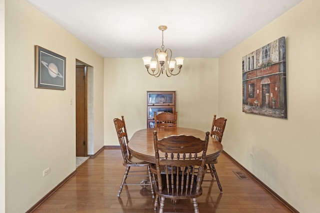 dining area featuring baseboards, wood finished floors, a notable chandelier, and visible vents