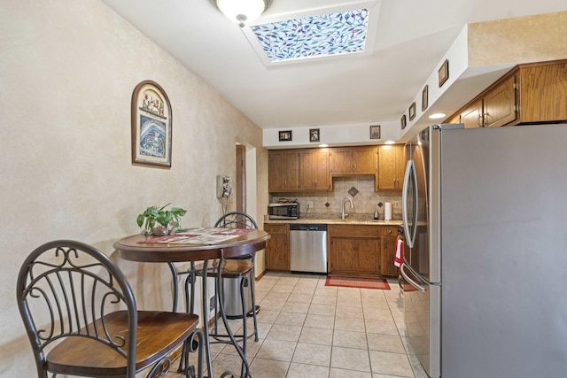 kitchen featuring light tile patterned floors, tasteful backsplash, light countertops, stainless steel appliances, and brown cabinets