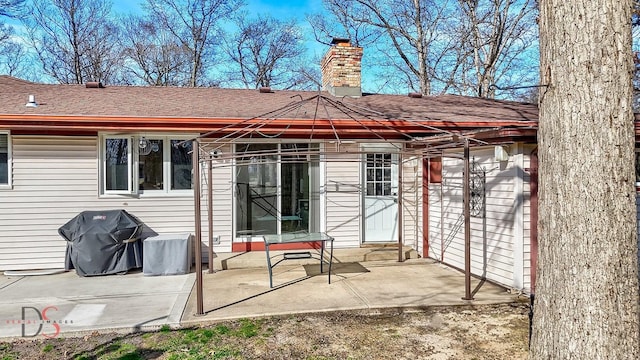 rear view of property featuring roof with shingles, a patio area, and a chimney