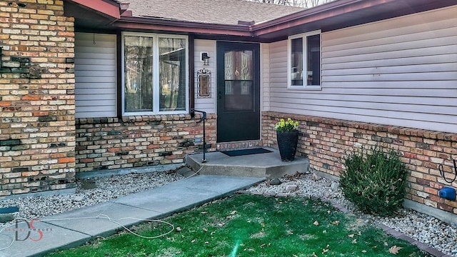 property entrance featuring brick siding and a shingled roof