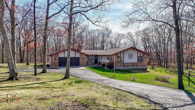 view of front facade with aphalt driveway, a chimney, a garage, brick siding, and a front lawn