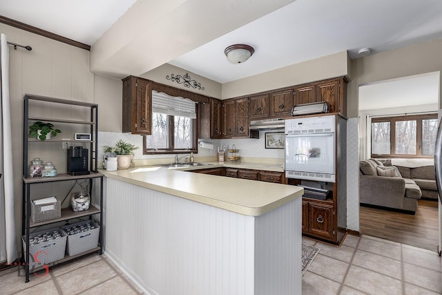 kitchen featuring light countertops, oven, backsplash, a peninsula, and dark brown cabinets