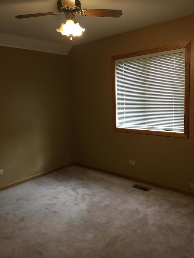carpeted spare room with baseboards, a ceiling fan, and visible vents