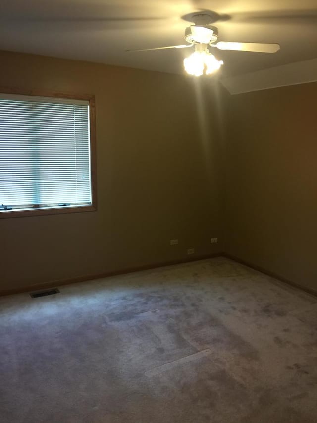 carpeted spare room with visible vents, a ceiling fan, and baseboards