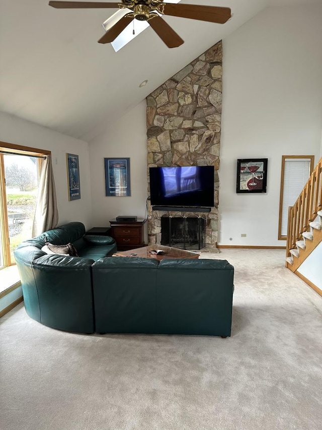 living room with high vaulted ceiling, stairway, a ceiling fan, a stone fireplace, and carpet flooring