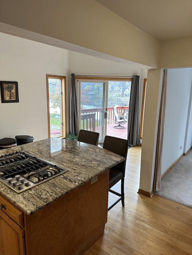 kitchen featuring dark stone counters, light wood-type flooring, baseboards, stainless steel gas stovetop, and brown cabinets