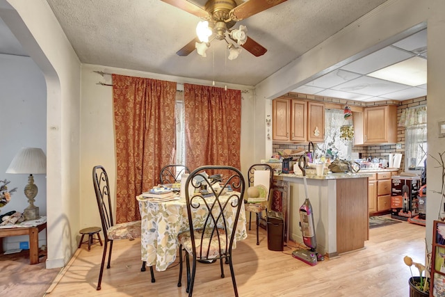 dining area with arched walkways, ceiling fan, a textured ceiling, and light wood-type flooring