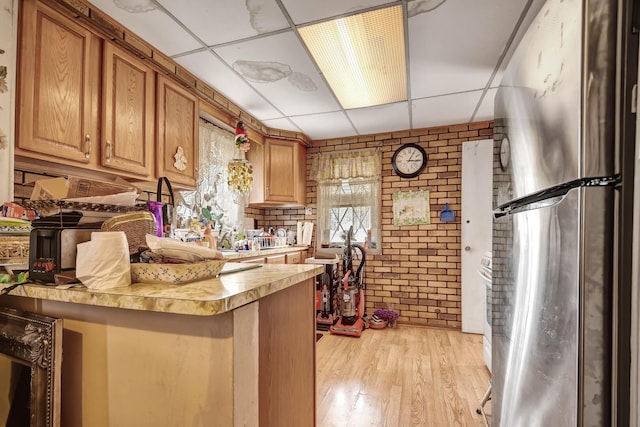 kitchen featuring light wood finished floors, light countertops, brick wall, a paneled ceiling, and freestanding refrigerator
