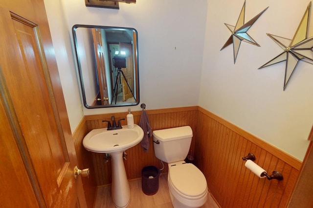 bathroom featuring wooden walls, wainscoting, a sink, and toilet