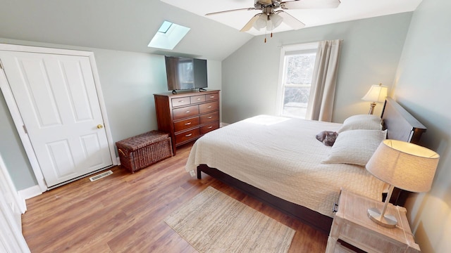 bedroom featuring vaulted ceiling with skylight, visible vents, ceiling fan, and wood finished floors