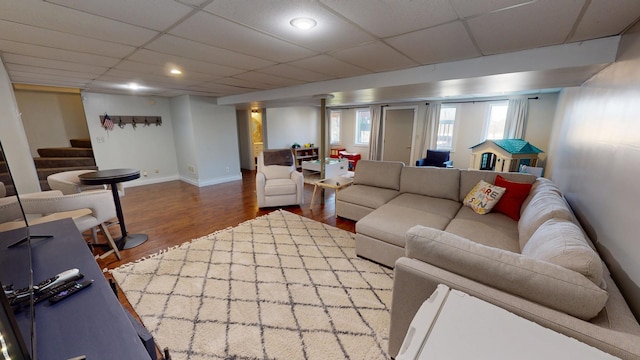 living area with baseboards, stairway, a paneled ceiling, and wood finished floors