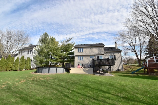 rear view of property with a yard, a deck, a covered pool, and a chimney