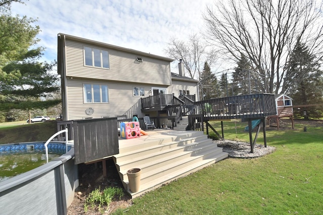 rear view of property featuring an outdoor pool, a deck, stairway, and a lawn